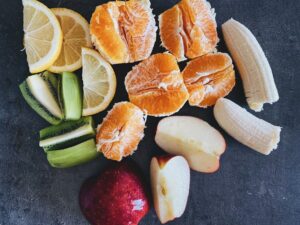 An arrangement of fresh fruits including oranges, apples, bananas, and lemons on a dark background.