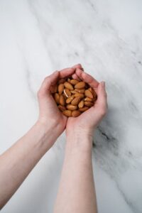 Two hands gently cupping a handful of almonds on a marble background, showcasing healthy snacks.