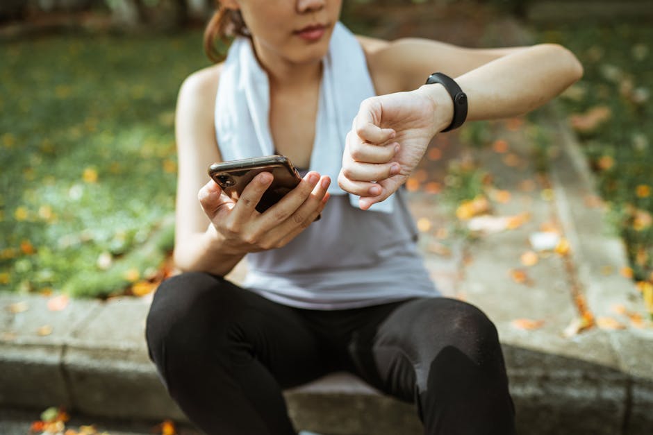 pexels-photo-4428992-4428992 Anonymous female in sportswear using smartphone and smart watch after exercising on sports ground