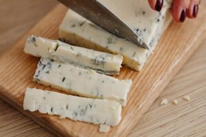 Close-up of slicing creamy gorgonzola cheese on a wooden board using a knife.