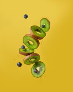 Slices of kiwi and blueberries suspended midair against a yellow backdrop.
